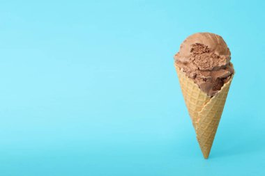 Delicious chocolate ice cream in waffle cone on light blue background. Space for text