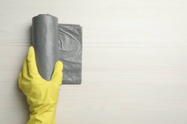Janitor in rubber glove holding roll of grey garbage bags on white wooden table, top view. Space for text