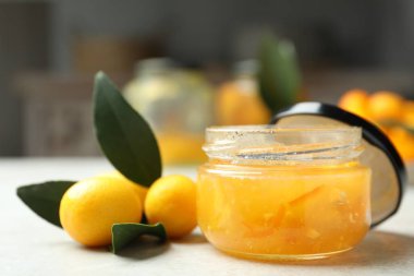 Delicious kumquat jam in jar and fresh fruits on white table, closeup