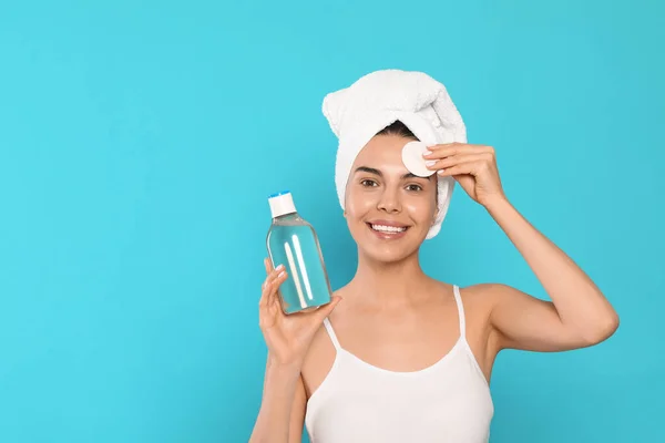 Young woman using cotton pad with micellar water on light blue background, space for text