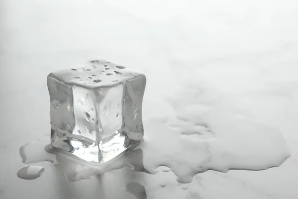 Wet ice cube on white table, closeup. Space for text