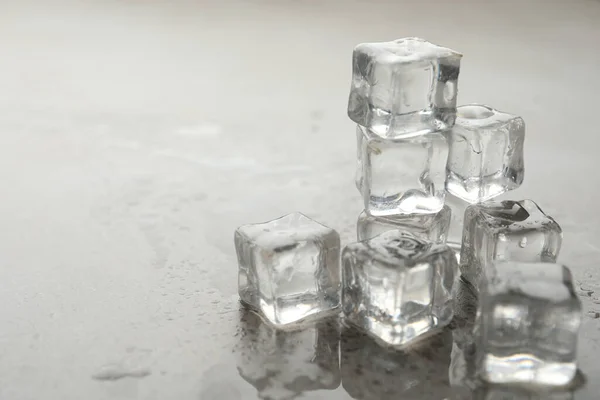 Crystal clear ice cubes with water drops on grey table, closeup. Space for text