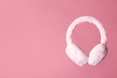 Stylish winter earmuffs on pink background, space for text