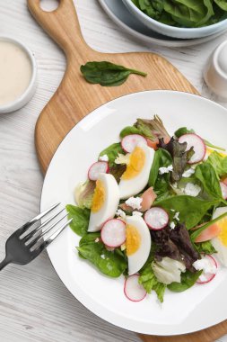 Delicious salad with boiled egg, radish and cheese served on white wooden table, flat lay