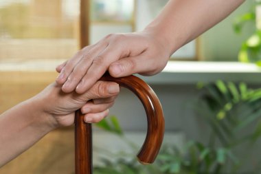 Caregiver and elderly woman with walking cane at home, closeup