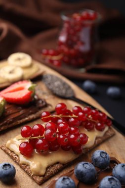 Fresh crunchy rye crispbreads with different toppings on wooden board, closeup