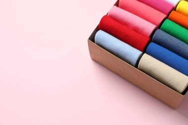 Box with different colorful socks on light pink background. Space for text