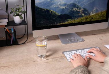 Woman working on computer at wooden table in room, closeup