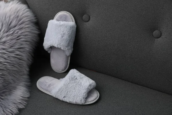Soft grey slippers and faux fur on sofa, space for text