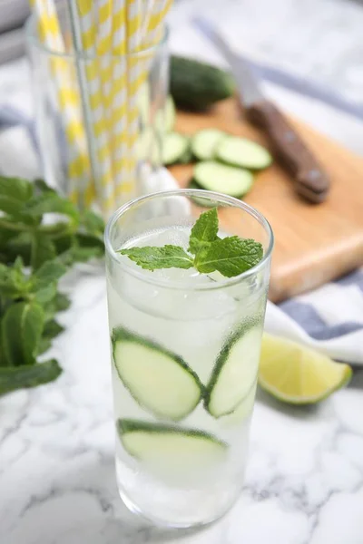 Glass of refreshing cucumber water with mint on white marble table