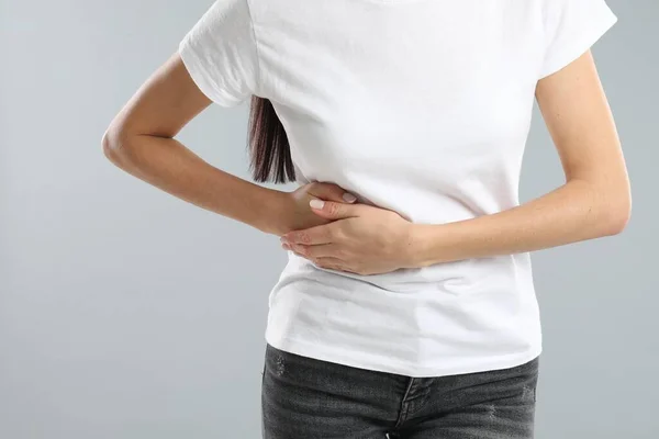 Woman suffering from liver pain on grey background, closeup