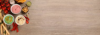 Different delicious hummuses on wooden table, flat lay with space for text. Banner design