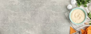 Delicious hummus and tortilla chips on light grey table, flat lay with space for text. Banner design