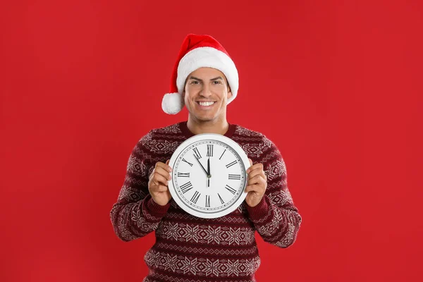 赤い背景の時計を着たサンタの帽子の男 新年のカウントダウン — ストック写真