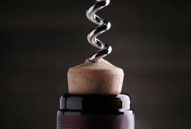 Opening wine bottle with corkscrew on dark background, closeup