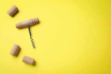 Corkscrew and wine bottle stoppers on yellow background, flat lay. Space for text