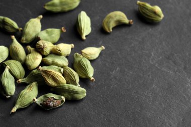 Pile of dry cardamom pods on black table, space for text