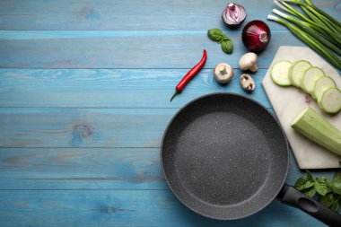 Flat lay composition with frying pan and fresh products on light blue wooden table, space for text