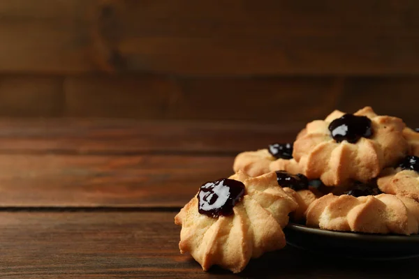 Tasty shortbread cookies with jam on wooden table. Space for text