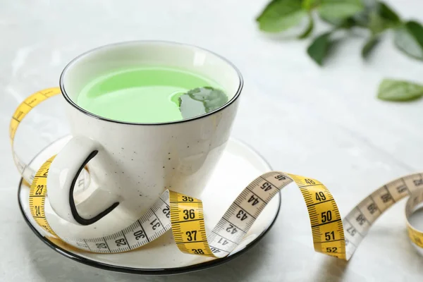 Cup of herbal diet tea and measuring tape on light table