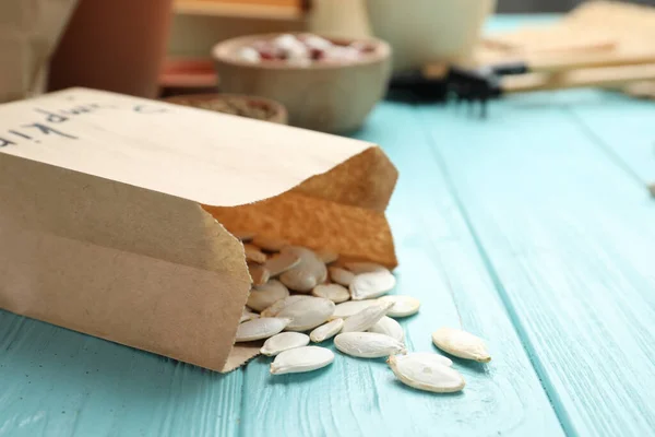 Paper bag with raw pumpkin seeds on blue wooden table, closeup. Vegetable planting