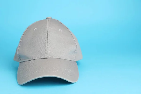 Stylish grey baseball cap on light blue background. Space for text