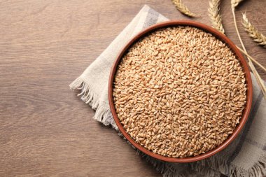 Wheat grains and spikes on wooden table, flat lay. Space for text