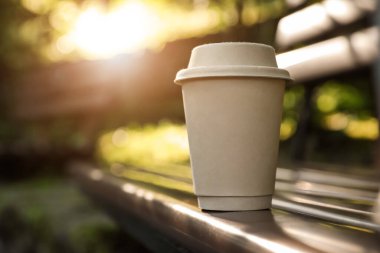 Cardboard takeaway coffee cup with lid on wooden bench outdoors, space for text