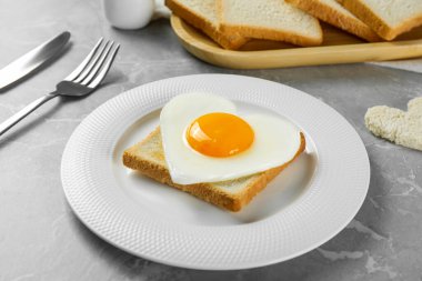 Heart shaped fried egg served on grey marble table