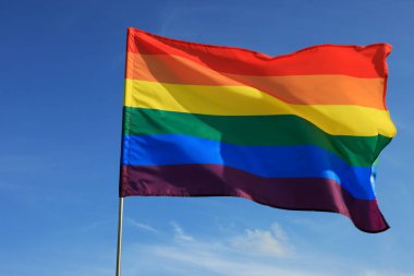 Bright LGBT flag fluttering against blue sky