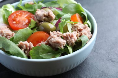 Bir kase lezzetli salata, konserve ton balığı ve siyah masada sebzeler, yakın plan.