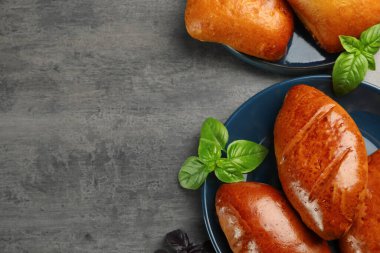 Delicious baked patties and basil on grey table, flat lay. Space for text