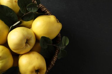 Fresh ripe organic quinces with leaves in wicker basket on black table, closeup. Space for text