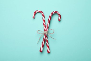 Two sweet Christmas candy canes with bow on turquoise background, top view