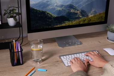 Woman working on computer at wooden table in room, closeup