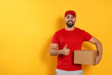 Courier holding cardboard box on yellow background, space for text