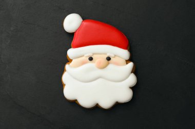 Santa Claus shaped Christmas cookie on black table, top view