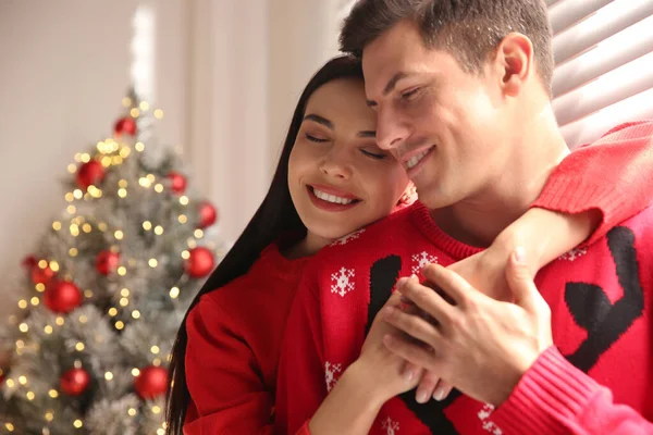 ハッピーカップルで暖かいセーター近くクリスマスツリー屋内 — ストック写真