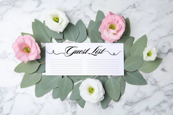 Fresh eucalyptus leaves, flowers and guest list on white marble background, flat lay