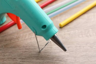 Turquoise glue gun and colorful sticks on wooden table, closeup