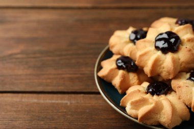 Tasty shortbread cookies with jam on wooden table, closeup. Space for text