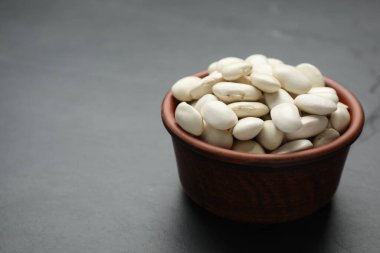 Raw white beans in bowl on black table. Space for text