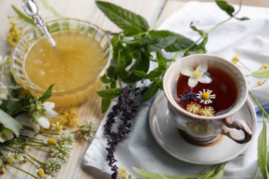 Cup of hot aromatic tea, honey and different fresh herbs on white wooden table