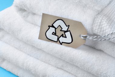 Stacked towels with recycling label on light blue background, closeup