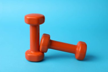Stylish orange dumbbells on light blue background
