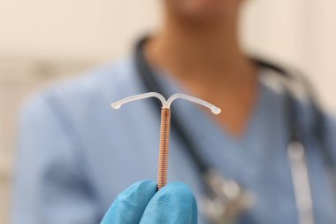 Doktor uterus içi doğum kontrol cihazını arka planda tutuyor. Yakın plan.