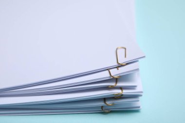 Sheets of paper with clips on light blue background, closeup