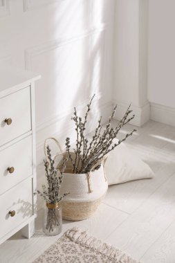 Pussy willow tree branches and pillow near chest of drawers in room
