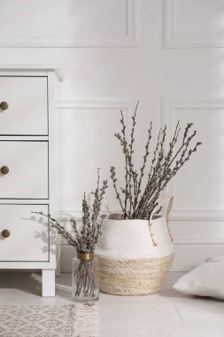 Pussy willow tree branches and pillow near chest of drawers in room