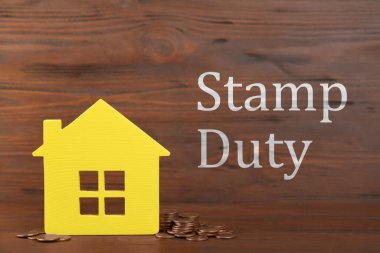 Stamp duty. House model and coins on wooden background